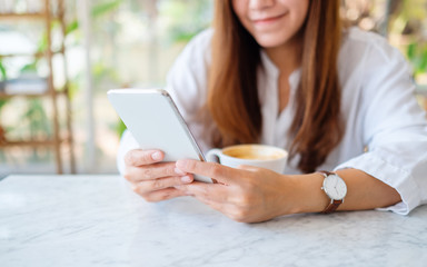Fototapeta premium Closeup image of a beautiful asian woman holding and using mobile phone with coffee cup on the table
