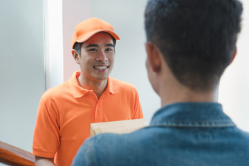 transportation same day delivery business concept. Smiled asian young delivery man send urgent package box to receiver / client on the door home with friendly attitude.