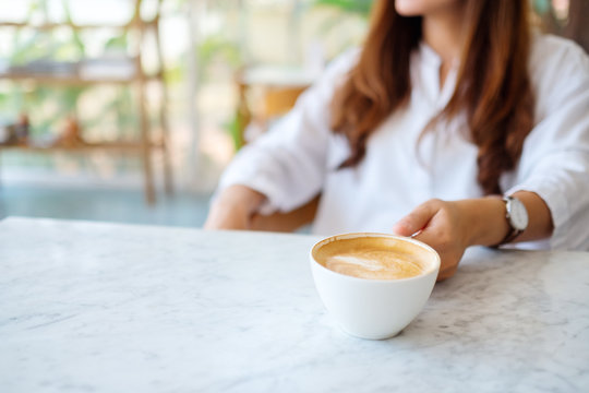 Closeup image of a woman grabbing a cup of hot coffee on the table