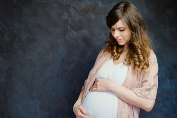 Fototapeta na wymiar Expectant mom touching her belly. Beautiful pregnant young woman on dark background. Copy space.