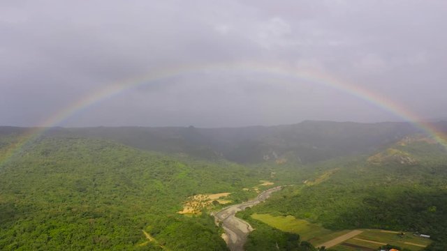 Rainbow in a mountain valley, after rain, top view. Summer and travel vacation concept. Mountains covered by rainforest, Luzon Island, Philippines.