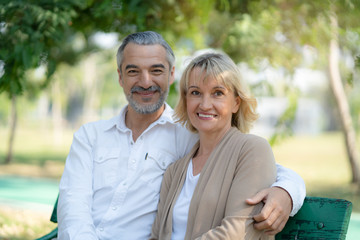 Obraz premium Elderly couple lifestyle concept. Husband embrace wife and sit on seat in the park relax on retirement life.