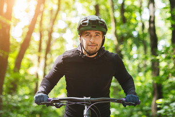 Serious bicyclist riding in sun light down forest path