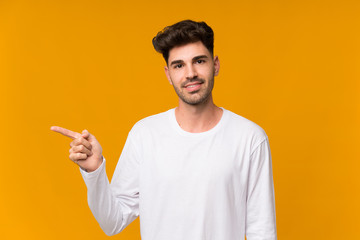 Young man over isolated orange background pointing finger to the side