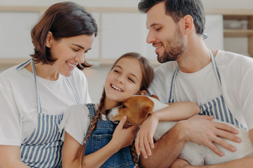 Obraz na płótnie Canvas Happy lovely family smile and express sincere emotions, enjoy spending time together at cozy home. Smiling little child glad parent bought her new pet, cuddle jack russell terrier with love and care.
