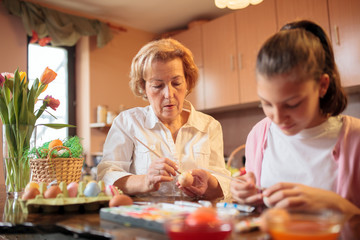 Senior Caucasian woman painting and decorating Easter eggs with her granddaughter in home kitchen