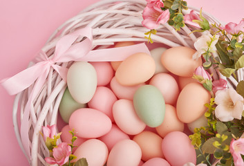 Colorful easter eggs in nest on pastel color background with flowers, copy space. Easter decorations. Easter background with painted eggs in nest, vintage style, top view. Spring greeting card
