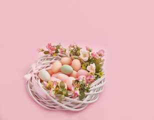 Colorful easter eggs in nest on pastel color background with flowers, copy space. Easter decorations. Easter background with painted eggs in nest, vintage style, top view. Spring greeting card