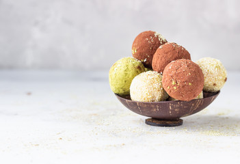 Homemade raw energy balls with matcha tea powder, cocoa powder and coconut flakes in a wooden bowl, light grey background. Selective focus. Vegan sweets. 