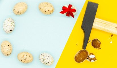 Happy easter creative card. Pop art style. Blue and yellow background. Seven eggs on one side, one with red bow and one smashed chocolate egg and metal hammer on another side. Close up. Copy space.
