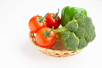 Fresh broccoli, green bell peppers and tomatoes in a basket on a white background