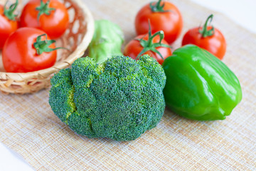 Fresh broccoli, green bell peppers and tomatoes in a basket and pepper shaker