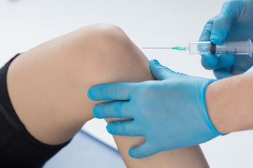The doctor puts an injection into the patient's knee joint. A shot in the knee