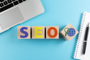 top view of letters SEO and internet search symbol on wooden cubes on blue background with laptop...