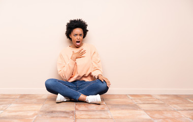 African american woman sitting on the floor surprised and shocked while looking right