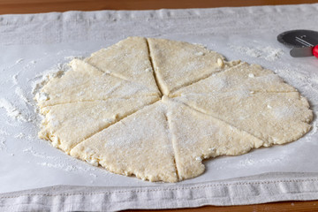Rolled raw curd dough with bits of cottage cheese cut into eight triangles sprinkled with sugar on baking paper on a linen tablecloth on a wooden table. The process of making curd bagels or croissants