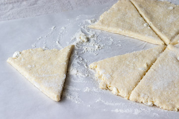 Rolled raw curd dough cut into eight triangles sprinkled with sugar and one triangle of dough lies separately on baking paper on a linen tablecloth. The process of making curd bagels or croissants