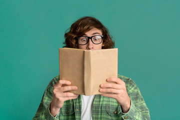 Education concept. Puzzled young man with glasses reading book on color background