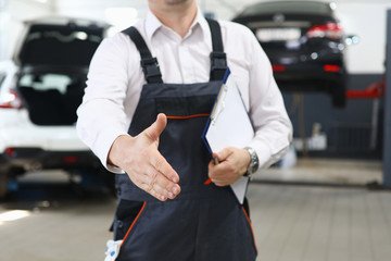 Close-up of professional car mechanic offer to shake hands with customer. Male worker holding checklist paper. Automobile service station and restoration workshop concept