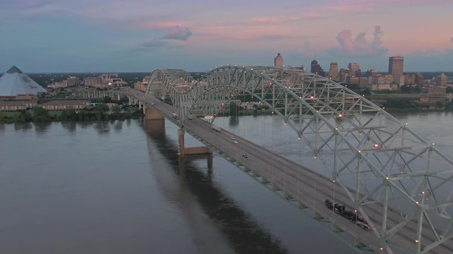Aerial flying over traffic on the Hernando de Soto Bridge that crosses the Mississippi River at sunset. In the background is downtown Memphis, Tennessee, USA
