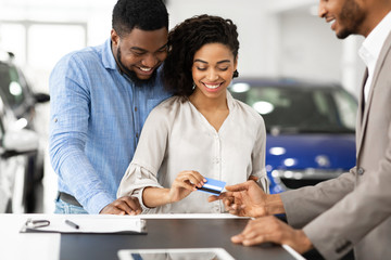 Spouses Giving Credit Card To Automobile Seller In Auto Showroom