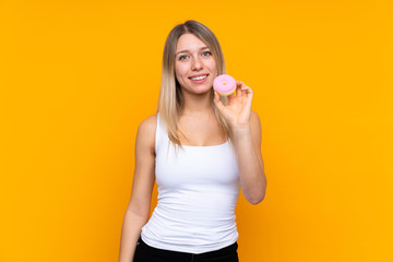 Young blonde woman over isolated blue background holding a donut and happy
