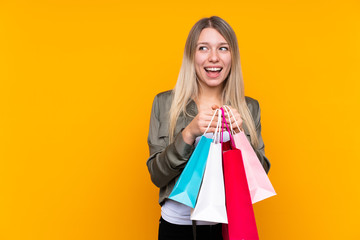 Young blonde woman over isolated yellow background holding shopping bags and surprised