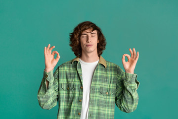 Harmony concept. Young man meditating or showing okay gesture on color background
