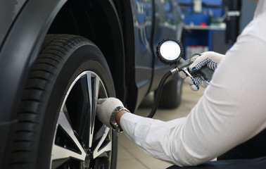 Close-up of male automechanic inflating tire and checking air pressure. Automobile wheel. Special...