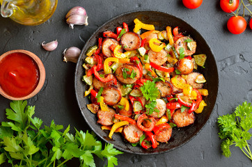 Slices of fried vegetables with sausages and spices in frying pan.