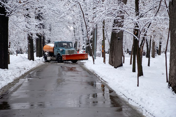 Truck is cleaning snow in park after snowfall. Snow blizzard snowstorm background. Industrial vehicle.