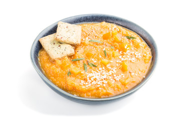 Sweet potato or batata cream soup with sesame seeds and snacks in blue ceramic bowls isolated on white background. side view, close up.