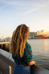 Fototapeta premium Blond girl with curly hair looking at the sunset by the sea in Barcelona, Catalonia, Spain.
