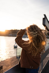 Blond girl with curly hair looking at the sunset by the sea in Barcelona, Catalonia, Spain.