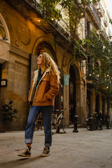 Obraz na płótnie Canvas Blond girl walking through the streets of the center of the city of Barcelona in Catalonia, Spain wearing a jacket and blue jeans. Looking up to the old buldings.