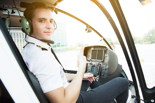 Portrait of young caucasian pilot with headset sitting in private airplane cabin flying.Handsome pilot in formal wear and headset sitting in helicopter cabin.Aircraft of transportation.