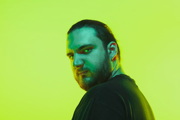 Portrait of a guy with colorful neon light on green studio background. Male model with calm and serious mood. Facial expression, cyberpunk, millenials lifestyle and look like. Future, technologies.