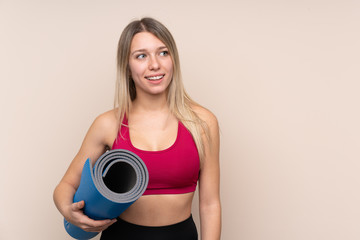 Young sport blonde woman over isolated background with a mat and smiling