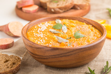 Sweet potato or batata cream soup with sesame seeds in a wooden bowl on a white wooden background. side view, selective focus.