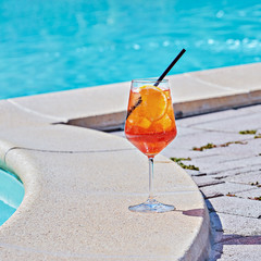 Wine Glass of cold cocktail Aperol spritz against turquoise water of poolside. Closeup of...