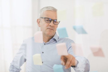 Elderly manager looking at sticky notes on window