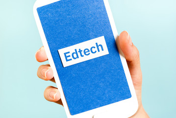 EdTech Education and Technology learning concept with a hand holding a paper phone on blue background.