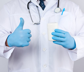 male doctor in a white medical coat and blue latex gloves holds a white plastic jar of pills