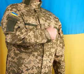 Ukrainian man a warrior dressed in a military pixel uniform stands against the background of the national flag of Ukraine