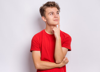 Portrait of pensive teen boy on grey background. Thoughtful teenager holding hand near face, looking seriously away at copy space. Beautiful caucasian confident child student. - 328086142