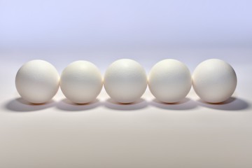 Five white chicken eggs lined horizontally side by side a blunt bottom round side forward center on a light background.