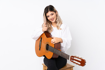 Teenager girl with guitar over isolated white background points finger at you with a confident expression