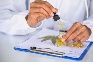 Researchers or doctors are about to drop CBD hemp oil in a glass bottle near a prescription. CBD Cannabis Oil Treatment Concept Natural herbs that extract oil for treatment