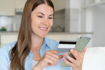 Young woman sit in living room use smartphone. Female housewife shopping online with credit card