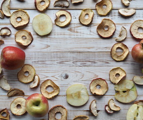 Use of dried fruits and vegetables. Dried apple chips and red fresh apples on a white wooden table. Organic natural wholesome food. Place for text. Top view.